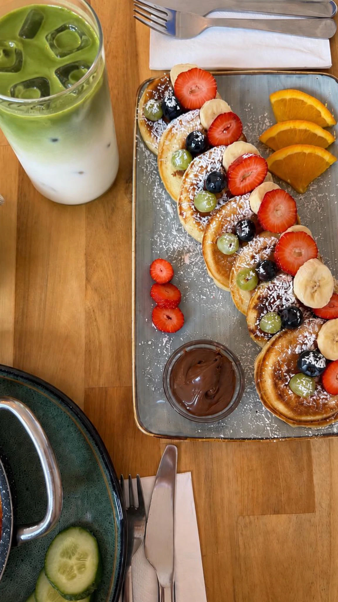 Pancakes mit frischen Beeren neben einem Iced Matcha